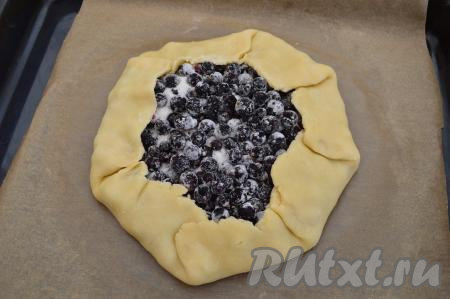 Переложить бумагу с раскатанным тестом на противень. Выложить в центр теста начинку из чёрной смородины. Завернуть края теста на начинку, сформировав открытую галету, как на фото.