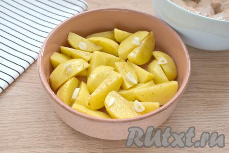 Перемешиваем картофель со специями и маслом, затем перекладываем в жаропрочную форму. Сверху на картошку кладём очищенные зубчики чеснока, нарезанные на пластины.