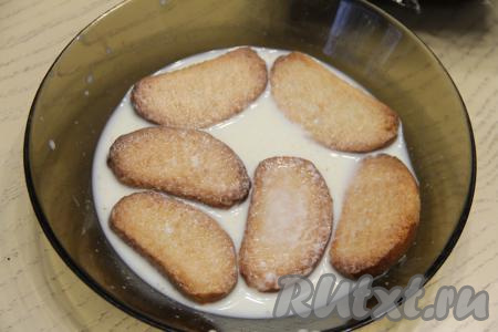 Дно и бока формы, в которой будете формировать торт (я взяла форму размером 11 сантиметров на 30 сантиметров), выстелить плёнкой. В достаточно объёмную миску влить 200 миллилитров молока. Выложить часть сухариков, оставить секунд на 30 (сухарики должны стать достаточно мягкими, но размокнуть и потерять форму они не должны).&nbsp;