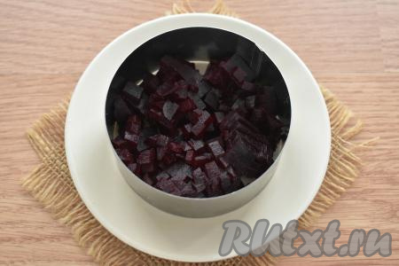 Картошку и морковь тщательно моем и, не очищая от кожуры, выкладываем в кастрюлю, заливаем полностью водой и отвариваем до готовности. В отдельной кастрюле отвариваем в кожуре до готовности свеклу. Варёным овощам даём остыть, а непосредственно перед формированием салата "Селёдка под шубой" очищаем их. Формировать салат слоями можно в общем салатнике. А я решила подать порционно, сформировав 2 порции салата, выкладывая каждую порцию в сервировочное кольцо диаметром 9 сантиметров, поставив его на плоскую тарелку. Поскольку слои в этом рецепте мы будем формировать в обратном порядке (в отличие от классического варианта), поэтому первым слоем выкладываем в кольцо половину свеклы, нарезанной на маленькие кубики. Вторую половину нарезанной свеклы выкладываем во второе кольцо.