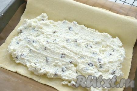 На одну половину раскатанного слоёного теста, отступив от краёв теста несколько сантиметров, выкладываем начинку из творога, разравниваем её, по-прежнему оставляя края пласта чистыми.
