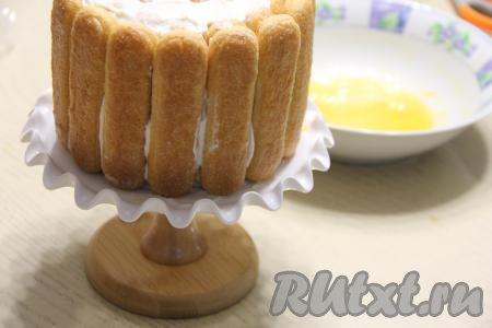 Начиная с ближайшего к вам печенья и помогая плёнкой, свернуть савоярди с кремом в рулет. Затем, сдвинув получившийся рулет из савоярди к себе, освободить край плёнки. На свободный край плёнки выложить одно за другим вплотную друг к другу оставшееся печенье, пропитанное мандариновым соком, смазать печенюшки кремом и продолжить сворачивать рулет. Свёрнутый рулет поставить на подставку (или на тарелку).