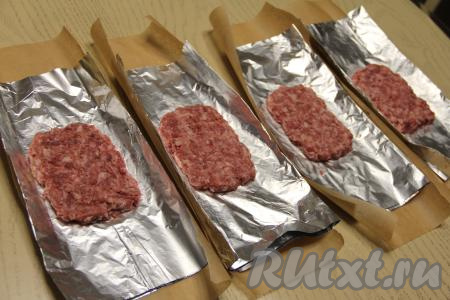 Для формирования формочки, в которой будем запекать котлету по-капитански, нужно отрезать кусок фольги, сложить пополам (форма из фольги, сложенной в 2 слоя, будет более прочной). На кусок фольги, сложенный вдвое, выложить одну часть фарша, сформировать прямоугольную котлету, как на фото. Аналогично сформировать на кусках фольги ещё 3 заготовки котлет. Кусочки фольги должны быть больше, чем мясная котлета. Я ещё дополнительно подстелила под фольгу примерно такой же по размерам кусок пергамента.