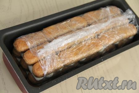 Примерно треть крема останется, нужно убрать его в холодильник. Накрыть верх тирамису свисающими краями плёнки и убрать в холодильник на ночь (или минимум на 5 часов).