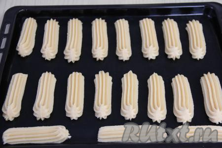 Переложить заварное тесто в кулинарный мешок с фигурной насадкой и отсадить в виде продолговатых эклеров на противень, предварительно застеленный ковриком (или пергаментом) для выпечки. Отсаживать тесто нужно на расстоянии друг от друга, так как эклеры увеличатся в размере в процессе выпечки.