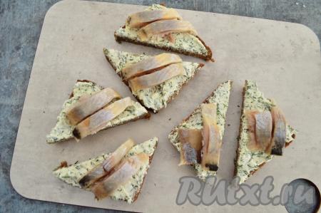 Филе сельди осмотреть, удалить косточки, если они есть. Нарезать филе селёдки на кусочки шириной 1-1,5 сантиметра. Выложить на каждый бутерброд по два кусочка селёдки.