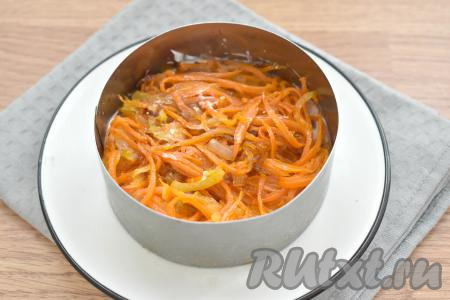 Следующим слоем равномерно раскладываем по двум кольцам обжаренные овощи. Утрамбовываем слой из лука и моркови ложкой. Смазывать этот слой майонезом не требуется.