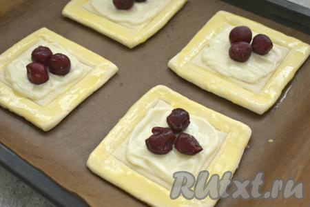 Таким образом формируем все слойки с творожным сыром и вишней, выкладываем их на противень, застеленный ковриком (или пергаментом) для выпечки. Яичный желток взбиваем вилкой. Смазываем края слоек взбитым желтком.