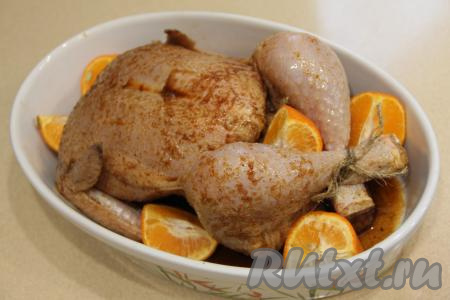 Выложить в форму с курицей оставшиеся мандарины, нарезанные на части. Накрыть форму с курицей фольгой и отправить в разогретую духовку. Запекать при температуре 180 градусов примерно 1 час. Затем снять фольгу и запекать ещё 30 минут (до готовности). Для того чтобы проверить готовность курицы, проколите её зубочисткой в районе бедра. Если из разреза выделяется прозрачный сок без примесей крови, значит птица готова. Курочка в процессе запекания покроется красивой и румяной корочкой.