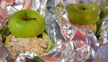 Наполнить творожно-яблочной начинкой яблоки, немного "утрамбовать" начинку руками. Накрыть яблоки "крышечками", завернуть их плотно в фольгу. Яблоки, фаршированные творогом и завёрнутые в фольгу, поместить в форму для запекания. На дно формы налить немного воды. Отправить яблоки запекаться в предварительно разогретую до 200 градусов духовку на 15-20 минут. За 5-7 минут до окончания запекания немного приоткрыть фольгу и запекать яблочки оставшееся время (до готовности). Запечённые яблоки должны стать достаточно мягкими, но при этом хорошо держать форму.