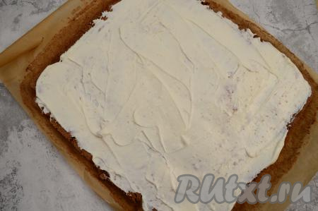 Развернуть шоколадный рулет, отделить от бумаги. Равномерно смазать корж с одной стороны творожным кремом.