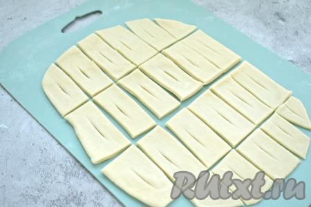 Острым ножом раскатанное тесто нарезаем на полоски размером 2 сантиметра на 4 сантиметра (или 3 сантиметра на 5 сантиметров). В центре каждой полоски делаем небольшой надрез.