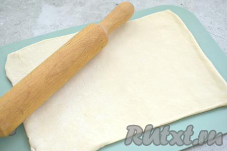 Для этой выпечки подойдёт как слоёное дрожжевое тесто (я его и купила), так и бездрожжевое слоёное тесто. Заранее достаём тесто из морозилки и оставляем оттаивать при комнатной температуре. Размороженное тесто кладём на стол, слегка присыпанный мукой. Немного раскатываем пласт теста скалкой в одном направлении (очень тонко раскатывать не нужно).