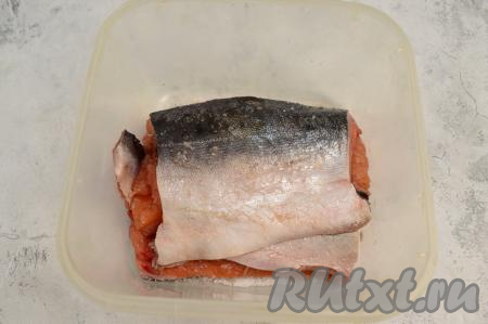 2 половинки каждого филе горбуши сложить друг на друга кожей наружу. Оба филе выложить в пластиковый контейнер (или в глубокую миску), закрыть крышкой и отправить на 2 суток в холодильник. Через сутки нужно будет перевернуть кусочки рыбы, а воду, выделившуюся в процессе сухой засолки, из контейнера нужно будет слить.