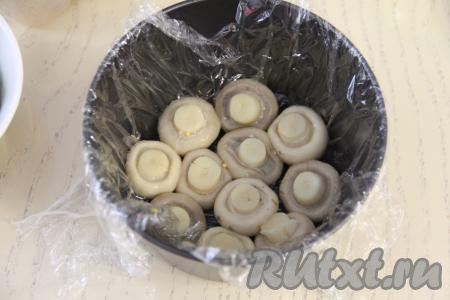 Форму (я взяла металлическую форму диаметром 13 сантиметров, но можно формировать и в глубокой миске или тарелке) застелить пищевой плёнкой так, чтобы края плёнки свисали с краёв формы. На дно формы выложить целые шампиньоны шляпками вниз (я выложила на дно формы 11 шампиньонов).&nbsp;