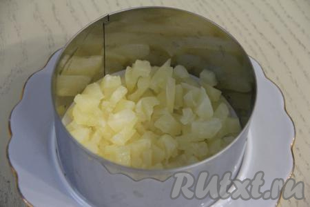 Кулинарное кольцо диаметром 12 сантиметров выставить на плоскую тарелку. Ананасы нарезать на мелкие кубики и выложить в кольцо первым слоем.