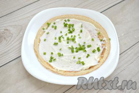 Даём блинчикам немного остыть. Зелень (я использовала зелёный лук, подойдёт также укроп или петрушка) моем, обсушиваем, нарезаем мелко. На каждый блин выкладываем примерно 2 чайных ложки творожного сыра и размазываем по всей поверхности. Сверху на творожный сыр добавляем немного нарезанной зелени. 