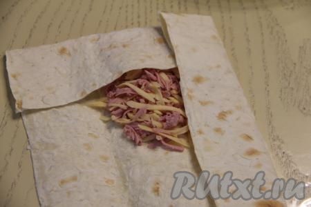 Вначале завернуть на начинку один край лаваша (я подвернула более узкий край), затем подвернуть на начинку боковые части лаваша, после этого свернуть лаваш с начинкой в виде конвертика, начиная с подвёрнутой (более узкой) части лаваша.