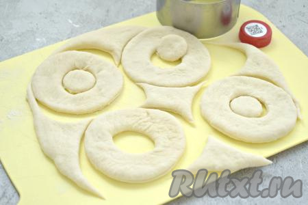 Поднявшееся дрожжевое тесто обминаем, делим на 2-3 куска. Каждый кусок теста на слегка присыпанной мукой поверхности раскатываем в пласт толщиной примерно 5-7 миллиметра. С помощью сервировочного кольца (у меня диаметр кольца 8 сантиметров) вырезаем кружки, в середине каждого кружка вырезаем крышкой от пластиковой бутылки отверстия. У нас получаются заготовки пончиков. Оставшееся тесто собираем в ком, раскатываем и тоже вырезаем из него заготовки пончиков. Из указанного количества ингредиентов у меня получилось 15 заготовок пончиков.