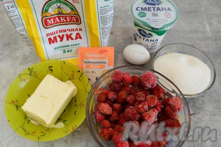 Подготовить продукты для приготовления песочного пирога с клубникой и сметанной заливкой. Сливочное масло следует заранее достать из холодильника, чтобы оно согрелось до комнатной температуры. Ягоды клубники можно взять как свежие, так и замороженные. Свежую клубнику нужно промыть водой, удаляя чашелистики, затем обсушить. Замороженные ягоды, если на них нет наледи, можно не размораживать.