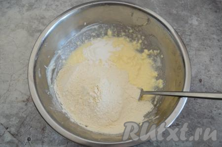 В миску с масляно-сметанной смесью всыпать разрыхлитель, добавить половину муки, перемешать до однородности. Затем понемногу добавлять оставшуюся муку, перемешивая тесто вначале вилкой, а когда тесто начнёт собираться в ком, продолжать его замешивать руками.