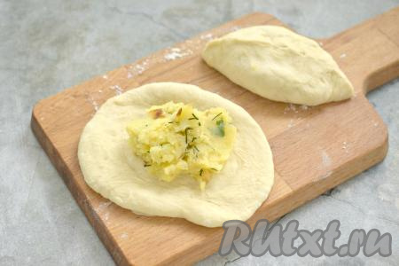 Поднявшееся тесто обминаем. Делим на 10-12 кусочков. Каждый кусочек на припылённой мукой поверхности раскатываем в нетонкую лепёшку. В центр каждой лепёшки кладём 2 столовых ложки картофельной начинки. Края лепёшки закрепляем над начинкой, формируя пирожок. Таким образом лепим все пирожки с картошкой.