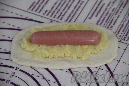 Сосиску разрезать вдоль пополам. На один пирожок будем добавлять половину сосиски. Выложить часть картофельного пюре на тесто, отступив по 1,5-2 сантиметра от краёв. Сверху на картофельное пюре выложить половинку сосиски.