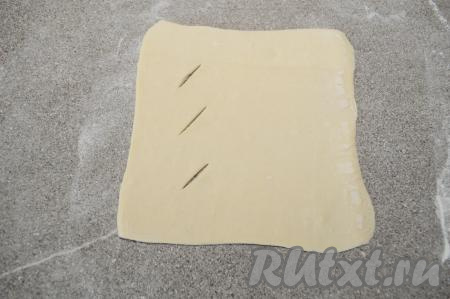 Рабочую поверхность присыпать мукой. Взять одну часть теста, раскатать в квадрат со стороной 15 сантиметров и толщиной 2 миллиметра. Ближе к левому краю квадрата, отступив от краёв, сделать 3 надреза ножом, как на фото.