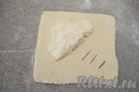 Ближе к противоположному углу выложить 1 столовую ложку начинки из творога и сыра. Разровнять начинку, придав форму треугольника, как на фото.