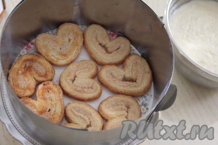 После того как крем хорошо охладится, можно будет приступать к формированию торта. Для этого нужно кулинарное кольцо (я взяла диаметром 19 сантиметров), установить на тортовницу (или на плоскую тарелку), выложить несколько штук слоёного печенья "Ушки" в один слой.