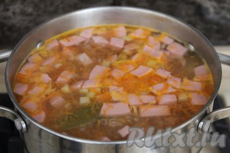 После того как картошка с рисом проварятся минут 15, добавить в кастрюлю колбасу, обжаренные овощи, лавровый лист, дать закипеть и варить суп на небольшом огне 5 минут.