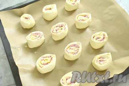 Выкладываем рулетики срезом вверх на противень, застеленный пергаментом. В небольшой ёмкости взбиваем яйцо вилкой, а затем смазываем яичной смесью верх и бока рулетиков.