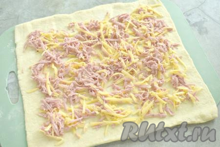 На раскатанный пласт теста, отступив от краёв по 1,5 сантиметра, равномерно выкладываем начинку из колбасы и сыра. 