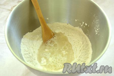 В углубление в мучной смеси вливаем тёплую воду (температура воды примерно 38-39 градусов) и растительное масло, перемешиваем лопаткой.