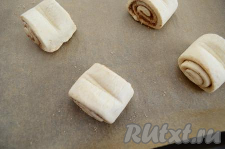 Переложить заготовку булочки с сахаром и корицей на противень, застеленный бумагой для выпечки. Аналогично сформировать все булочки из оставшихся полосок слоёного теста (всего у нас получатся 4 булочки среднего размера) и тоже выложить на противень. Выкладывать заготовки слоек нужно на расстоянии друг от друга.