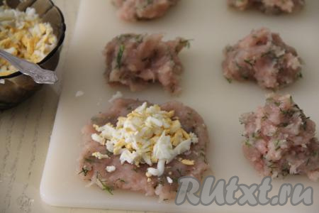 Из одной части фарша сформировать лепёшку, в центр выложить одну часть натёртых яиц.