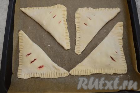 Выложить заготовки слоёных пирожков на противень, застеленный пергаментом. Выкладывать слойки с клубникой нужно на небольшом расстоянии друг от друга. Сырое яйцо в небольшой ёмкости взболтать вилкой до однородности. Смазать яйцом пирожки и отправить выпекаться в разогретую до 200 градусов духовку на 20 минут.