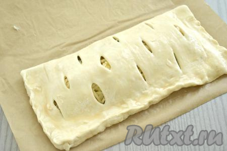 Накрываем начинку из грибов и сыра стороной теста с надрезами, плотно скрепляем края. Яйцо в небольшой ёмкости взбиваем вилкой до однородности. Смазываем поверхность слоёного пирога взбитым яйцом.