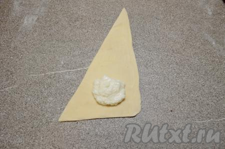 Ближе к основанию треугольной заготовки, отступая от краёв ориентировочно по 1,5 сантиметра, выложить 1,5-2 чайных ложки творожной начинки.