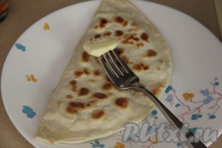 Готовую лепёшку с творогом и зеленью переложить со сковороды на тарелку, сразу смазать сливочным маслом с двух сторон. Таким образом приготовить все тонкие турецкие лепёшки.