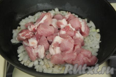 Прогреть в глубокой сковороде растительное масло, выложить мелко нарезанный лук, обжарить его на среднем огне до прозрачности (на это потребуется минуты 3-4), иногда перемешивая. Затем добавить в сковороду кусочки свинины, перемешать.