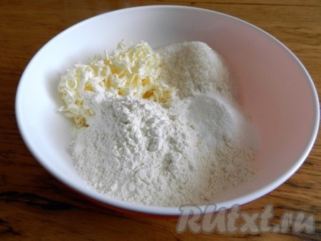 Сливочное масло достать из холодильника, натереть на крупной тёрке в глубокую тарелку, добавить сахар, муку и разрыхлитель.