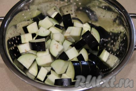 Баклажаны нарезать на средние кубики. В миску влить 500 миллилитров холодной воды, всыпать 0,5 столовой ложки соли, перемешать, выложить нарезанные баклажаны, перемешать и оставить минут на 30. Затем откинуть баклажаны на сито, промыть холодной водой, лишней воде дать стечь, оставить на несколько минут, чтобы баклажаны немного обсохли. В процессе замачивания и промывания из баклажанов уйдёт горечь, которая зачастую бывает в этих овощах.&nbsp;