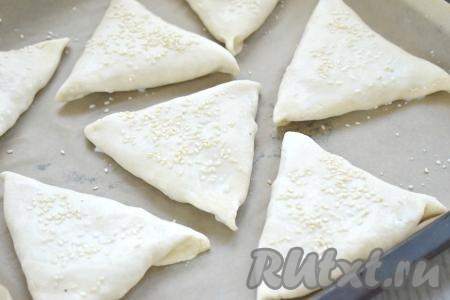 Самсу из слоёного теста с курицей и картошкой выкладываем "швом" вниз на противень, застеленный пергаментом (или ковриком) для выпечки. Аналогично формируем ещё 6 заготовок самсы и тоже выкладываем их на противень. Тесто смазываем молоком (можно смазать и взбитым яйцом) и посыпаем кунжутом.