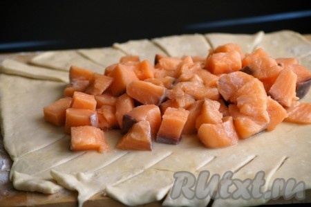 В центр раскатанного теста, оставляя края пустыми, выложить кусочки нарезанной форели. Тесто надрезать с длинных краёв так, как показано на фото.
