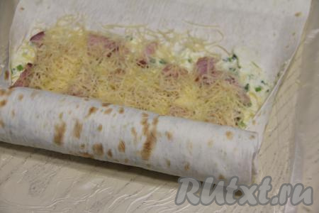 Слегка подвернуть длинные стороны лаваша на начинку, а затем свернуть лаваш в плотный рулет, начиная со стороны с начинкой. У нас получится, что в конце будет сделано несколько оборотов чистым листом лаваша.