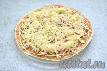 Натираем сыр и равномерно посыпаем им начинку пиццы на тортилье.&nbsp;