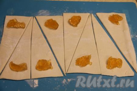 На широкий край каждого треугольника, отступив около 1,5 сантиметров от края, выложить по 1 чайной ложке джема. Джем лучше брать густой, чтобы начинка не вытекала во время выпечки рогаликов. Если у вас негустой джем (или варенье), тогда его можно смешать с небольшим количеством крахмала. В этом рецепте из двух пластов теста я сформировала 16 рогаликов, соответственно мне потребовалось 16 чайных ложек джема (по 1 чайной ложке на рогалик), поэтому для загущения негустого джема (или варенья) нужно будет добавить половину чайной ложки крахмала.