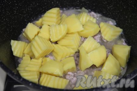 К луку, обжаренному с фаршем, выложить нарезанную картошку, влить 150 миллилитров воды, перемешать.