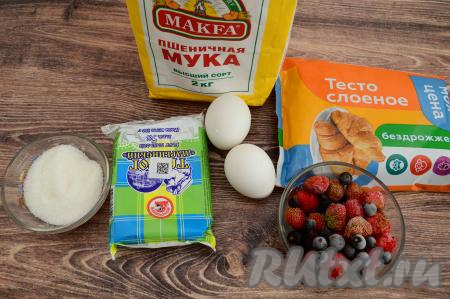 Подготовить продукты для приготовления пирога с творогом и ягодами из слоёного теста. Слоёное тесто для этого открытого пирога можно взять как дрожжевое, так и бездрожжевое. Я взяла бездрожжевое. Тесто разморозить при комнатной температуре. Ягоды можно взять как свежие, так и замороженные. Я взяла замороженную клубнику и чёрную смородину. Замороженные ягоды можно не размораживать, если на них нет большого количества наледи. Свежие ягоды нужно будет промыть, обсушить, разложив их на бумажном полотенце.